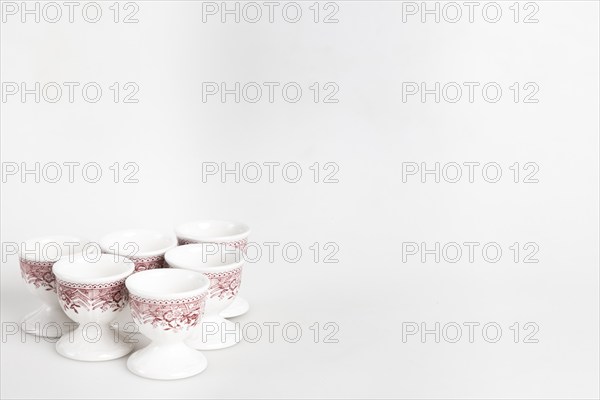 A set of white and red ceramic egg cups with a floral pattern arranged on a light-coloured