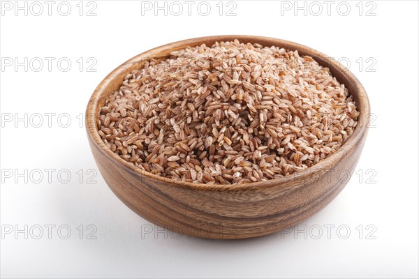 Wooden bowl with unpolished brown rice isolated on white background. Side view, close up