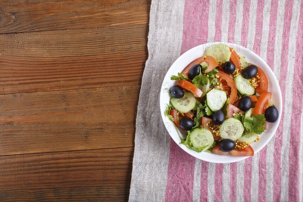 Vegetarian salad of tomatoes, cucumbers, parsley, olives and mustard on linen tablecloth, top view,