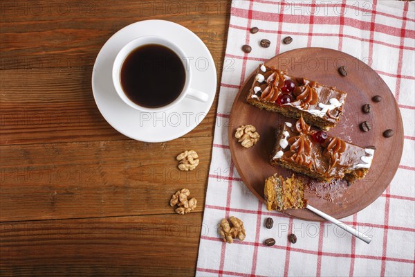 A piece of cake with caramel cream on a wooden kitchen board and a cup of coffee, brown wooden