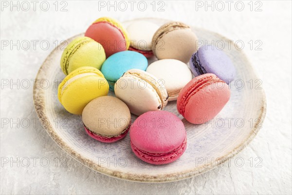 Multicolored macaroons on ceramic plate on gray concrete background. side view, still life, close