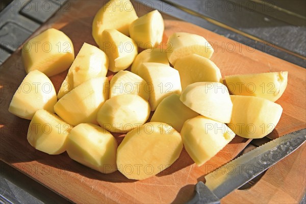 Peeled cut chopped potatoes on chopping board with kitchen knife