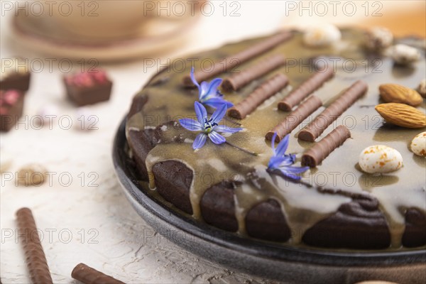 Homemade chocolate brownie cake with caramel cream and almonds with cup of coffee on a white