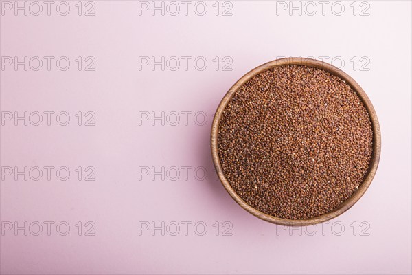 Wooden bowl with raw red quinoa seeds on a pastel pink background. Top view, flat lay, copy space