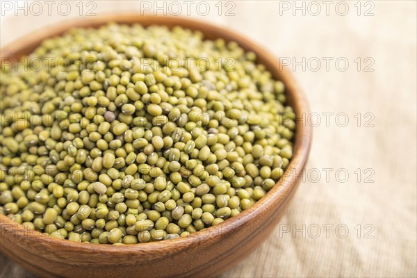 Wooden bowl with raw green mung bean on a white background and linen textile. Side view, close up,