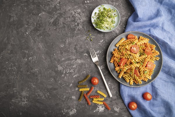 Tortiglioni semolina pasta with tomato and microgreen sprouts on a black concrete background and