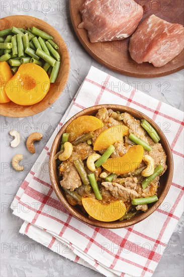Fried pork with peaches, cashew and green beans on a black concrete background. top view, close up,