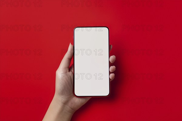 Female hand holding mobile phone with white empty screen in front of red background. KI generiert,