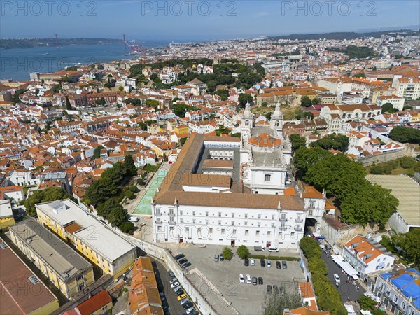 Aerial view of a coastal town with red roofs, white buildings, a bridge and green trees, aerial