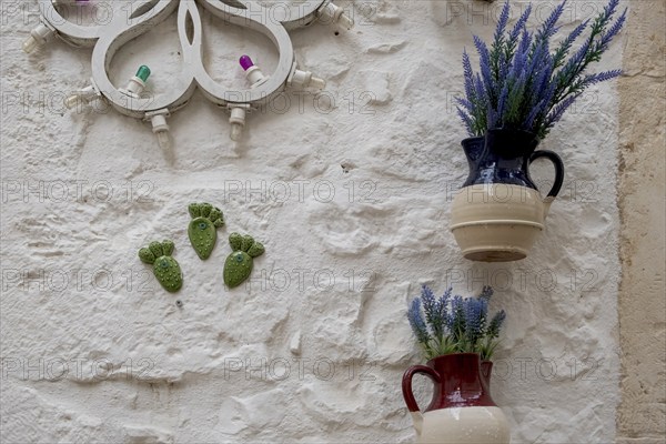 Jugs with artificial flowers hanging as decoration on a white house wall, Cisternino, Valle