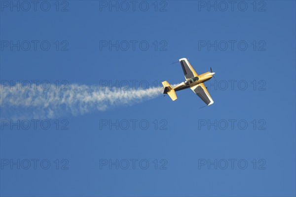 Golden stunt aerobatic plane performing stunts in blue sky with smoke trail. Concept of speed,