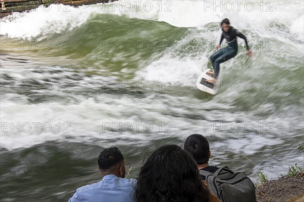 Surfer riding Eisbach wave, onlookers on the shore, Eisbach and wave in the English Garden are