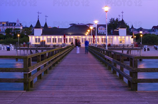 Illuminated pier with strolling people and buildings in the evening light, calm evening mood on the