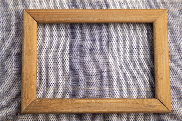 Wooden frame on smooth brown and violet linen tissue. Top view, flat lay, natural textile