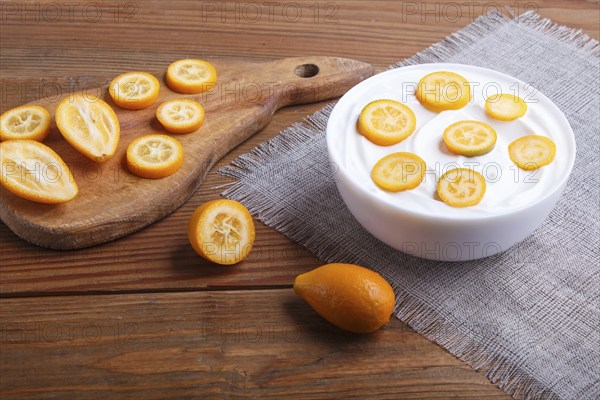 Greek yogurt with kumquat pieces in a white plate on a brown wooden background, close up