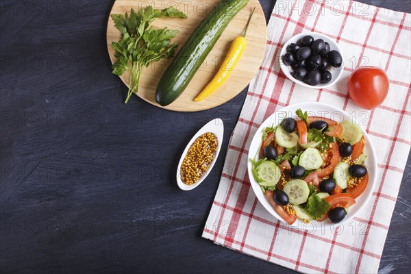Vegetarian salad of tomatoes, cucumbers, parsley, olives and mustard on linen tablecloth and black