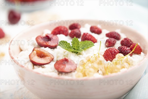 Rice flakes porridge with milk and strawberry in ceramic bowl on white concrete background and blue