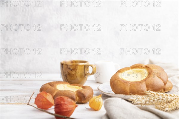 Sour cream bun with cup of coffee on a white wooden and concrete background and linen textile. Side