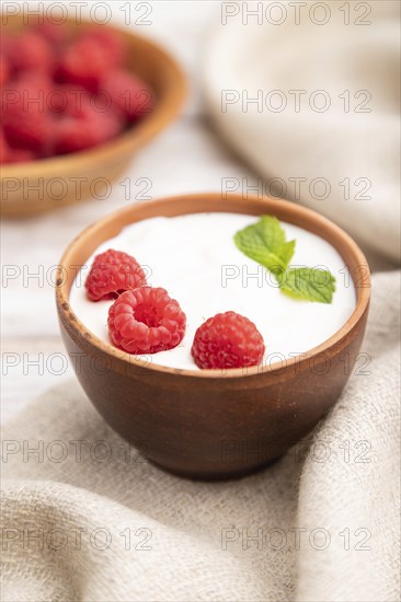 Yogurt with raspberry in clay cups on white wooden background and linen textile. Side view, close