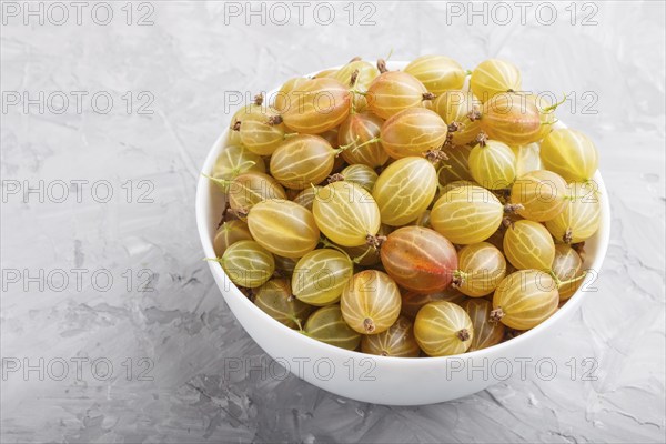 Fresh green gooseberry in white bowl on gray concrete background. side view, close up