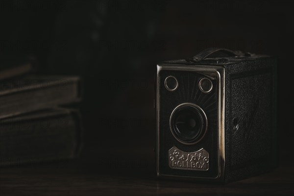 Old box camera against a dark background next to old books