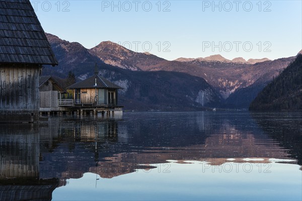 Lake Grundlsee in autumn at sunset. Boathouses on the left, mountains in the background. Blue sky,