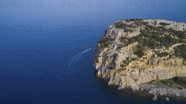 Drone shot, boat sailing along a rocky cliff over the clear blue sea, Anthony Quinn Bay, Vagies