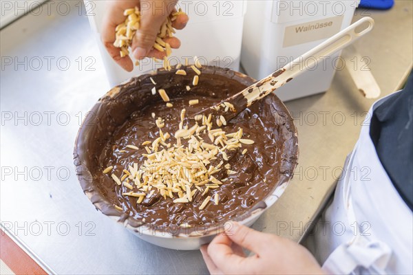 Almonds are added to a dark chocolate mixture in a bowl, Production Burch Schokolade, Haselstaller