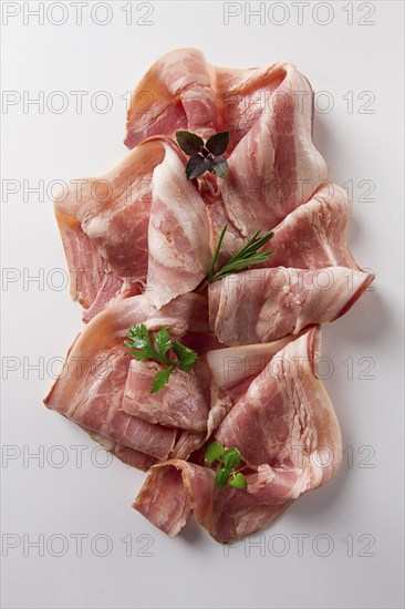 Raw bacon, sliced, with micro greenery and spices, on a white background, close-up