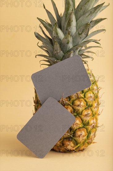 Gray paper business card with ripe pineapple on orange pastel background. Side view, copy space.