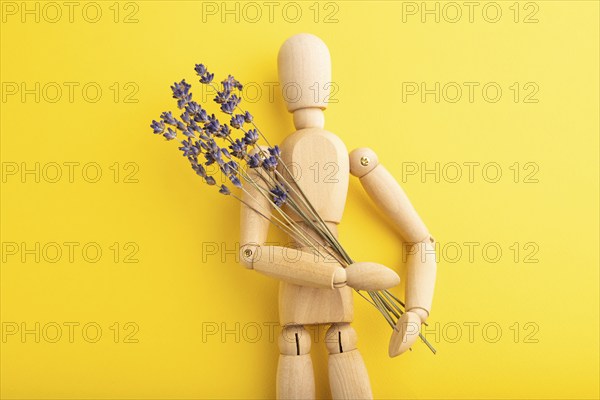 Wooden mannequin holding lavender flowers on yellow pastel background. copy space, isolated,