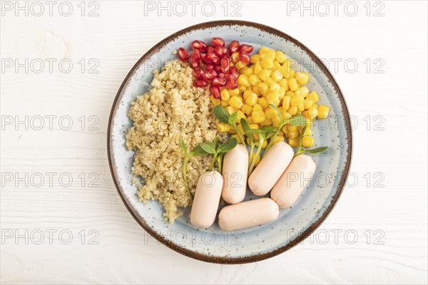 Mixed quinoa porridge, sweet corn, pomegranate seeds and small sausages on white wooden background.