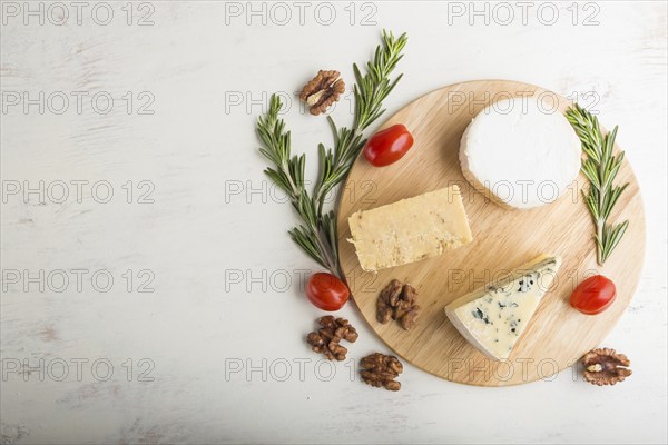 Blue cheese and various types of cheese with rosemary and tomatoes on wooden board on a white