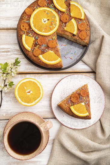 Orange cake and a cup of coffee on a white wooden background and linen textile. Top view, flat lay,