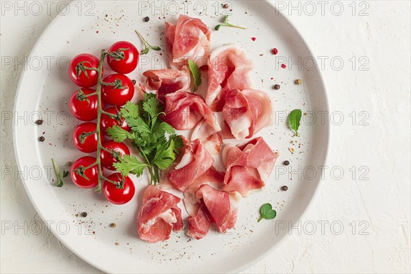 Sliced prosciutto, appetizer, with cherry tomatoes, on a white plate, top view