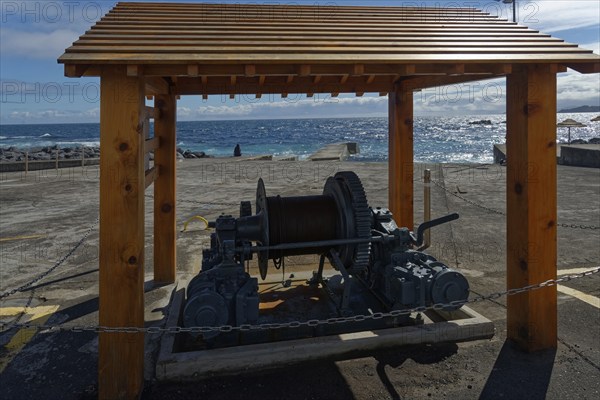 Historic whale towing facility and winch under a wooden canopy with a view of the sea and blue sky,
