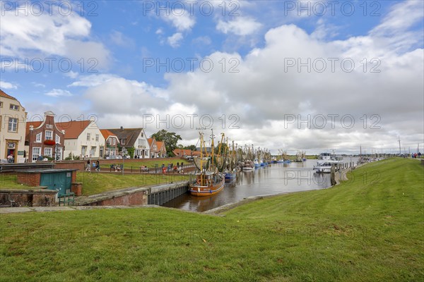 View of historic houses with colourful facades at the old harbour of Greetsiel, with fishing boat,
