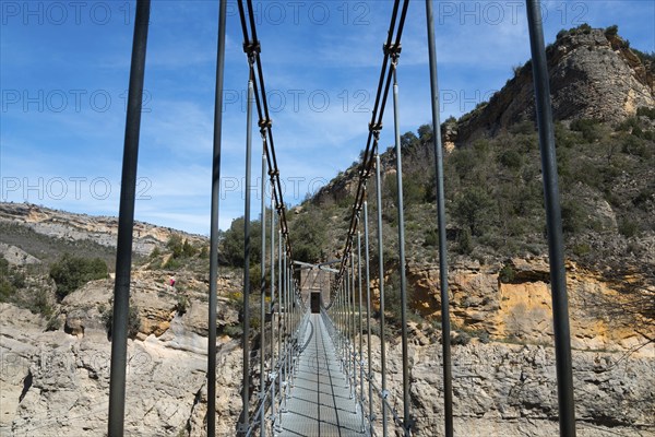 A suspension bridge leads through a rocky gorge with steep walls and green vegetation, Noguera