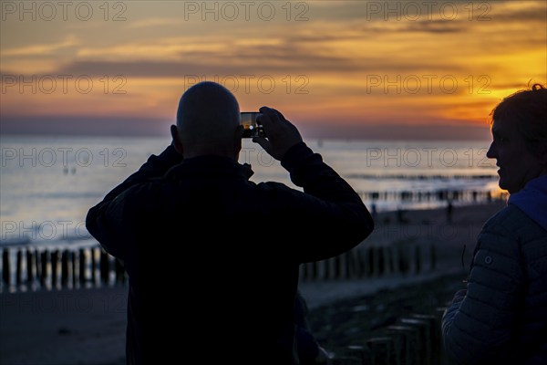 Sunset on the beach of Zoutelande, beach with wooden pile breakwaters, tourists, Zeeland,