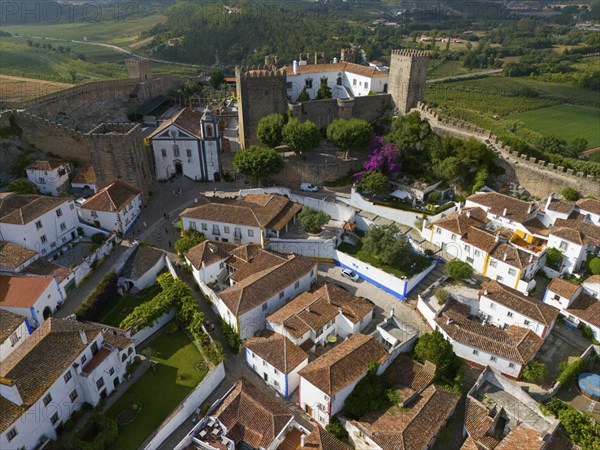 Aerial view of a medieval town with white houses and red tiled roofs, surrounded by city walls and