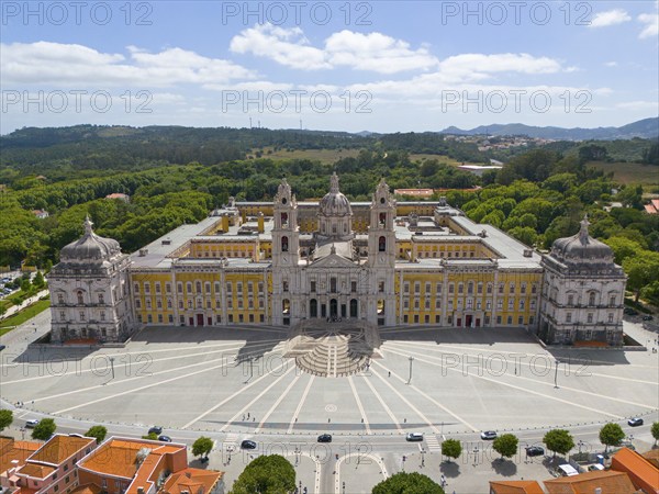 Aerial view of a baroque palace with symmetrical design, surrounded by a green landscape and