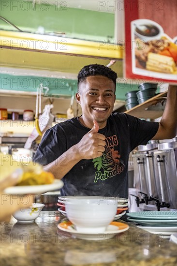 Vendor at a food stall shows thumbs up, looks into the camera, Mercado Central de San José, San
