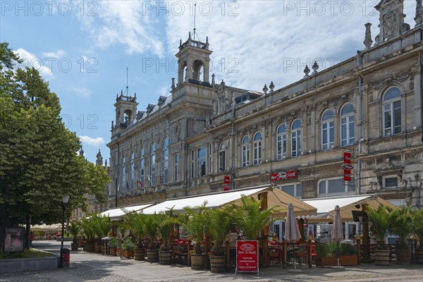 A street café in front of a historic building on a sunny day with blue sky and clouds, Drama