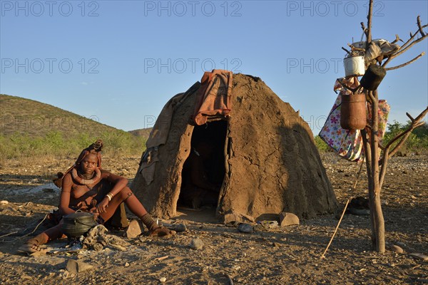 Young Himba woman sitting at a campfire in front of her hut, Ombombo, Kaokoland, Kunene, Namibia,