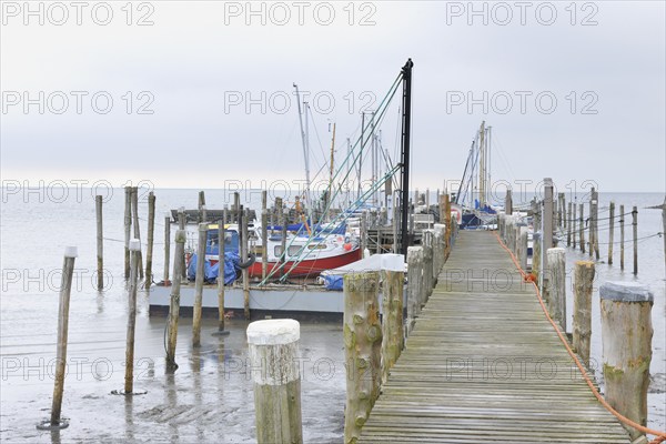A wooden dock extends out into the water with fishing boats moored alongside under a misty, cloudy
