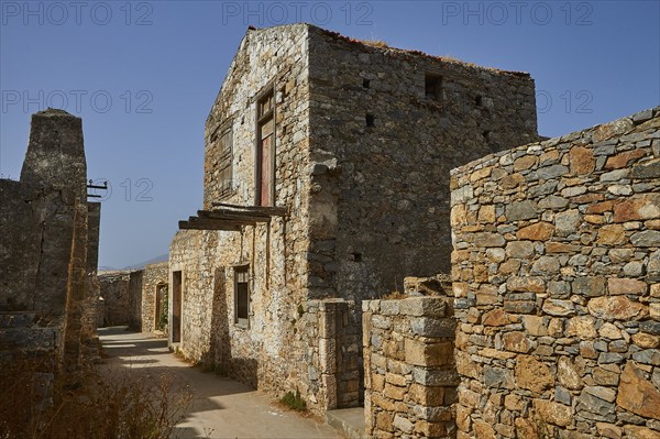 Old stone buildings in an abandoned village under clear skies with visible ruins, Venetian sea
