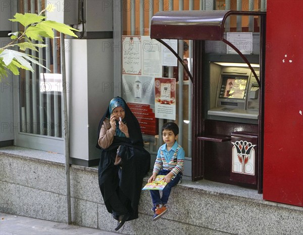 A mother sits with her child next to an ATM in Tehran, 17/05/2016