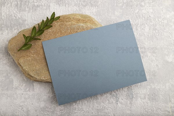 Blue paper business card, mockup with natural stone and boxwood branch on gray concrete background.