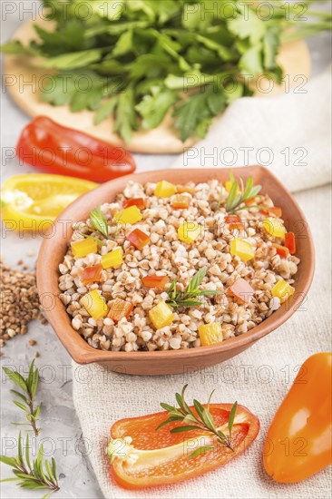Buckwheat porridge with vegetables in clay bowl on a gray concrete background and linen textile.