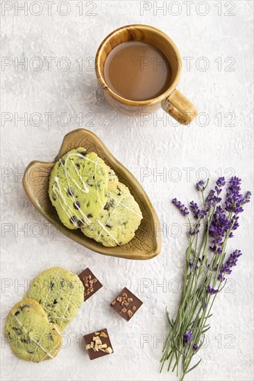 Green cookies with chocolate and mint on leaflike ceramic plate with cup of coffee on gray concrete